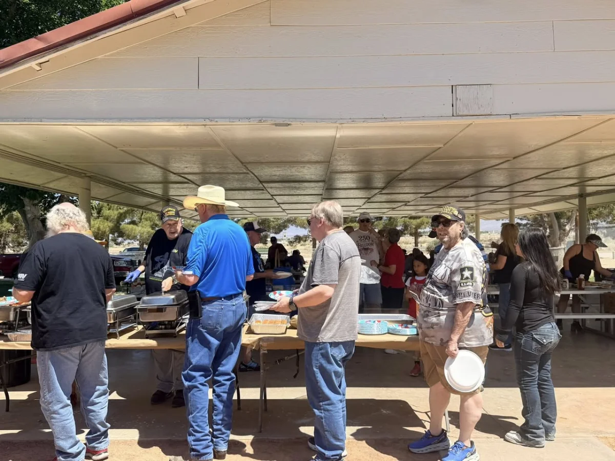 Chapter members serve food at an outdoor picnic under a pavilion, with a line of attendees holding plates.